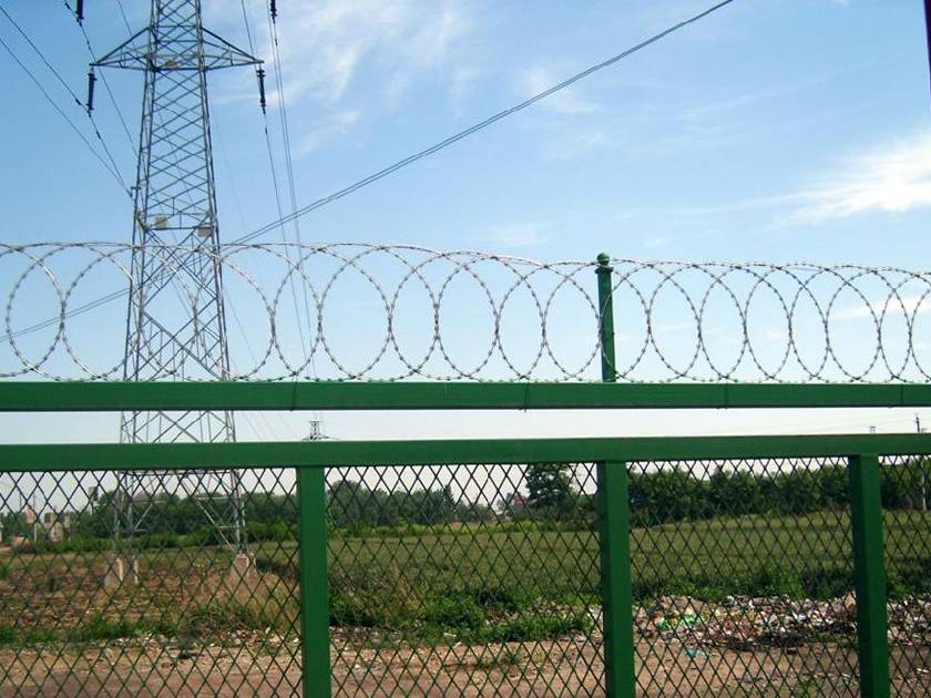 Flat wrap razor wire is installed at the top of expanded metal fence nearby the farmland.