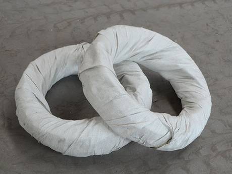 Two rolls of concertina razor wire in woven bag package on the ground.